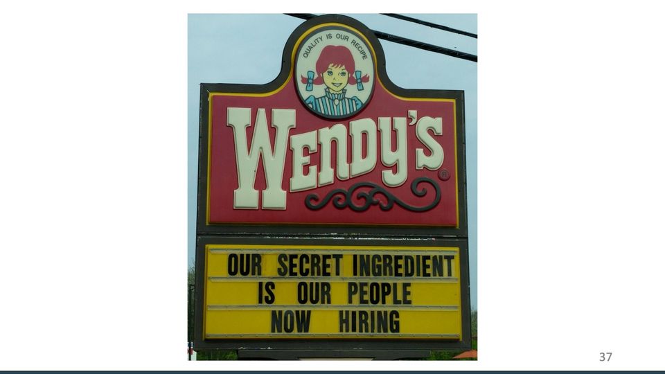 Photo of a Wendy's restaurant sign: a red logo panel with a red-pigtailed cartoon girl, above a yellow marquee of black letters.